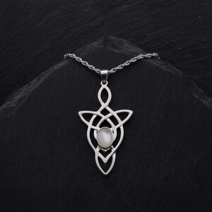 Puede incluir: Un collar de plata con un colgante de nudo celta con una piedra de n&aacute;car blanco en el centro.