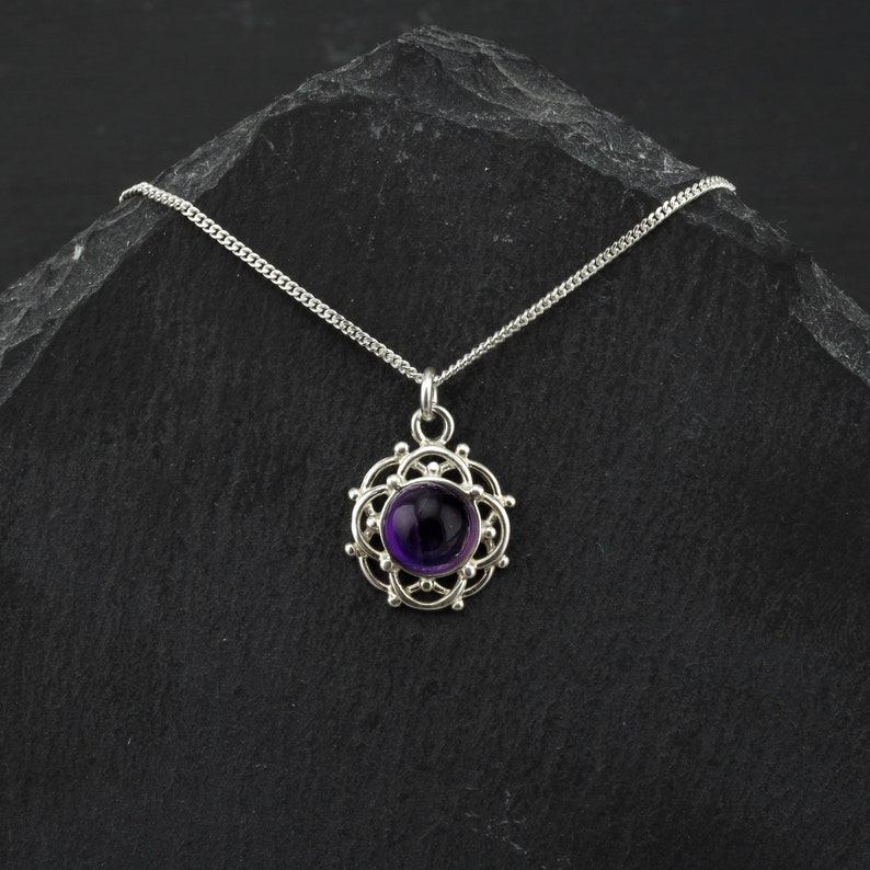May include: A silver necklace with a purple amethyst gemstone pendant set in a delicate silver filigree design.