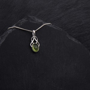 May include: A silver chain necklace with a green gemstone pendant. The pendant is in a Celtic knot design.