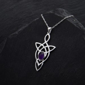 Puede incluir: Un collar de plata con un colgante de nudo celta con una amatista p&uacute;rpura en el centro. El collar est&aacute; sobre un fondo negro.