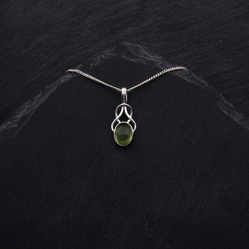 May include: A silver chain necklace with a green gemstone pendant. The pendant is in the shape of a Celtic knot.