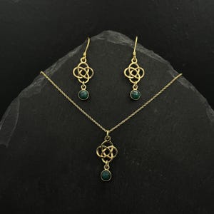 Pode incluir: Um conjunto de colar e brincos de ouro com um design de nó celta e detalhes de pedras preciosas verdes.