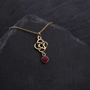 May include: A gold necklace with a Celtic knot pendant and a dangling red gemstone.