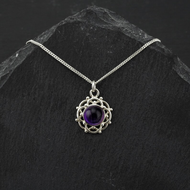 May include: A silver necklace with a purple amethyst gemstone pendant set in a delicate silver filigree design.