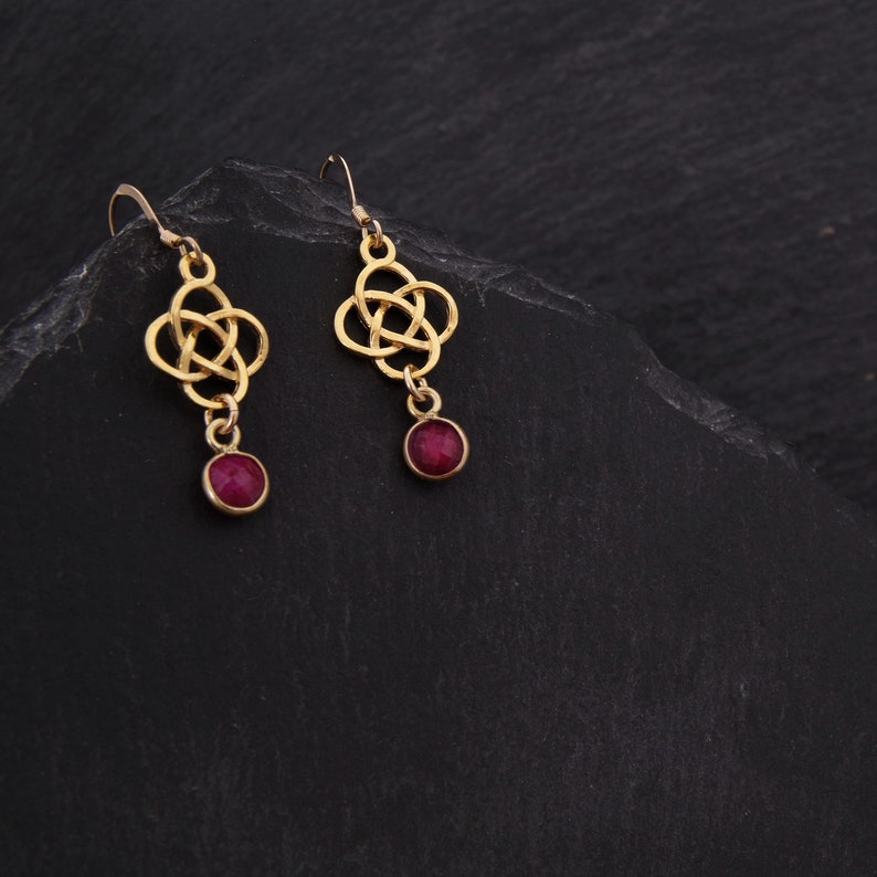 May include: A pair of gold earrings with a Celtic knot design and a dangling red gemstone.