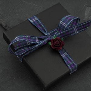May include: A black gift box with a plaid ribbon and a small red flower.