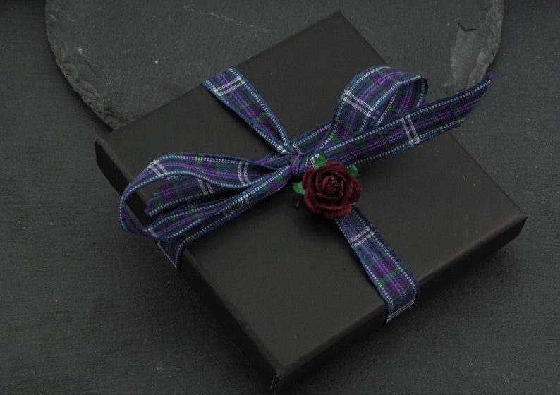 May include: A black gift box with a plaid ribbon and a small red flower.