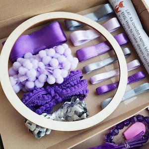 May include: A craft kit with a wooden hoop, ribbons, pom-poms, and trim in shades of purple, lavender, and silver. The kit includes a printed paper with text in multiple languages. The kit is designed for making dream catchers.