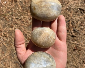 May include: Three smooth, polished moonstone stones in various sizes. The stones are a light gray color with iridescent shimmer.