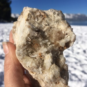 May include: A close-up of a rock with a cluster of clear quartz crystals embedded in it. The rock is a light brown color and the crystals are translucent.