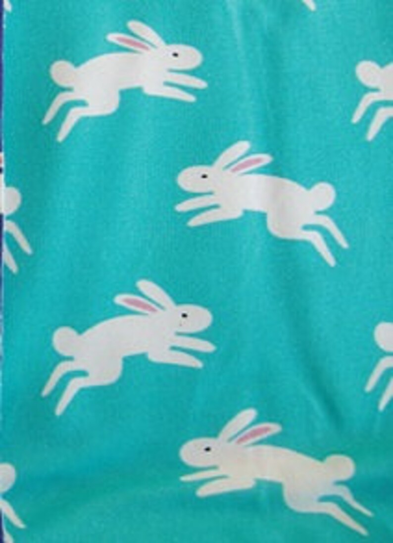 May include: A turquoise fabric with a repeating pattern of white rabbits in a running pose. The rabbits have pink inner ears and black eyes. The fabric is likely cotton or a similar material, suitable for quilting or crafting projects.