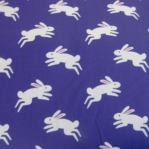 May include: A pattern of white rabbits with pink ears on a deep purple background. The rabbits are depicted in a running pose, creating a playful and whimsical design. This fabric is suitable for various craft projects.