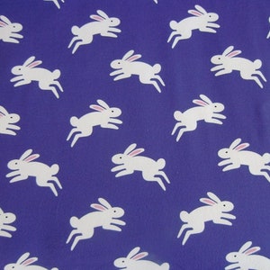 May include: A repeating pattern of white rabbits with pink ears on a deep blue background. The rabbits are depicted in a running pose, creating a playful and whimsical design. This pattern is suitable for fabric or wallpaper.