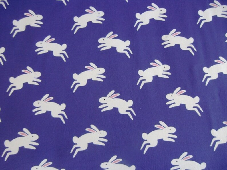 May include: A repeating pattern of white rabbits with pink ears on a deep blue background. The rabbits are depicted in a running pose, creating a playful and whimsical design. This pattern is suitable for fabric or wallpaper.
