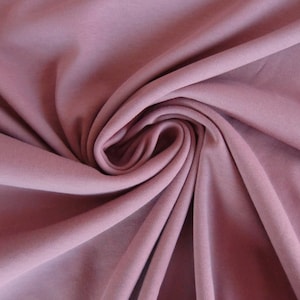 Può includere: Primo piano di un tessuto morbido di colore malva con una texture liscia. Il tessuto è drappeggiato e piegato, creando un aspetto morbido e fluido.
