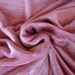 K&ouml;nnte beinhalten: Ein weicher, pl&uuml;schiger rosa Stoff mit einer strukturierten, flauschigen Oberfl&auml;che. Der Stoff ist gefaltet und drapiert und erzeugt einen weichen und einladenden Look.