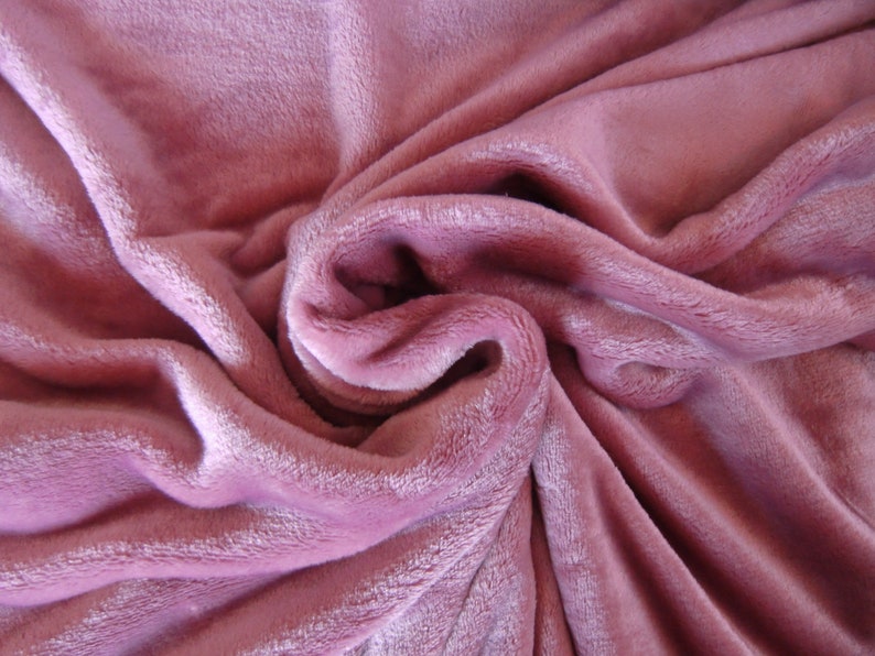 K&ouml;nnte beinhalten: Ein weicher, pl&uuml;schiger rosa Stoff mit einer strukturierten, flauschigen Oberfl&auml;che. Der Stoff ist gefaltet und drapiert und erzeugt einen weichen und einladenden Look.