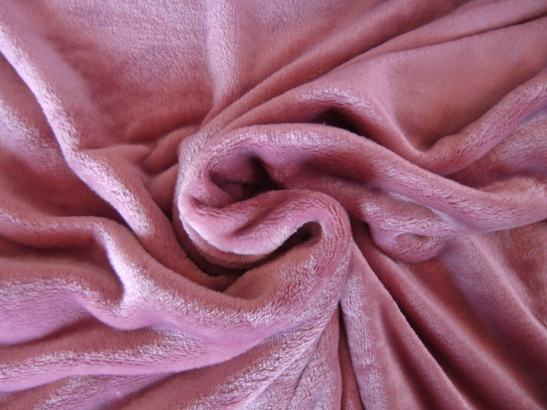K&ouml;nnte beinhalten: Eine weiche, pl&uuml;schige rosa Decke mit einer strukturierten Oberfl&auml;che. Die Decke ist gefaltet und drapiert, um ihre Textur und Farbe zu zeigen.