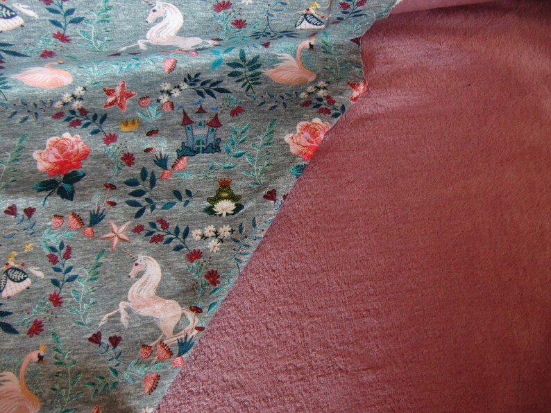 K&ouml;nnte beinhalten: Nahaufnahme von zwei Stoffproben. Die obere Probe ist ein grauer Stoff mit einem sich wiederholenden Muster aus rosa Flamingos, wei&szlig;en Einh&ouml;rnern und Blumendesigns. Die untere Probe ist ein einfarbiger, staubiger rosafarbener Stoff.