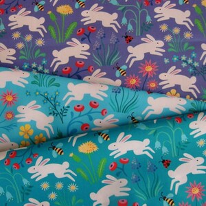 May include: Two fabric swatches with a repeating pattern of white bunnies hopping through a field of flowers. The top swatch is a light purple background with pink, yellow, and blue flowers. The bottom swatch is a turquoise background with yellow, pink, and blue flowers.