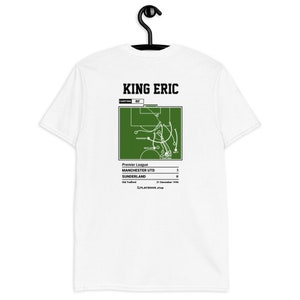 Puede incluir: Camiseta blanca con un diagrama de juego de fútbol verde y el texto "KING ERIC" impreso en la espalda. El diagrama muestra una jugada de fútbol de un partido de la Premier League entre Manchester United y Sunderland el 21 de diciembre de 1996. El marcador es de 5-0 a favor del Manchester United.