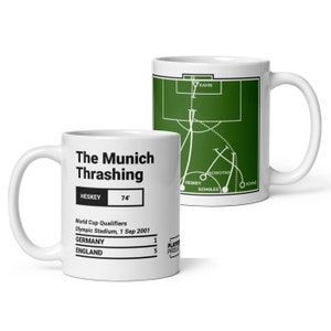 Puede incluir: Dos tazas blancas, una con un gráfico de campo de fútbol verde y la otra con un gráfico blanco que dice "The Munich Thrashing". El texto en la taza dice "World Cup Qualifiers Olympic Stadium, 1 Sep 2001 Germany 1 England 5"