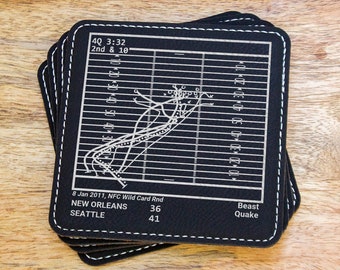 Könnte beinhalten: Ein Stapel schwarzer quadratischer Untersetzer mit weißen Nähten. Jeder Untersetzer zeigt ein weißes Football-Spielschema mit Yard-Linien und Text: "40 3:32 2nd & 10", "8 Jan 2011, NFC Wild Card Rnd", "NEW ORLEANS 36", "SEATTLE 41" und "Beast Quake".