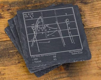 Könnte beinhalten: Ein Set quadratischer, dunkelgrauer Schieferuntersetzer mit einem eingravierten weißen Football-Spielzugdiagramm. Der Text lautet 4Q 0:19 4th & 5, 4 Jan 2006, Nat'l Championship, 1 USC 38, 2 TEXAS 41 und The Greatest Game Ever in weißer Schrift.