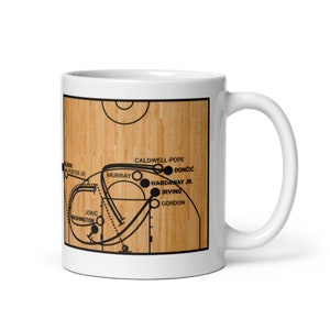 Könnte beinhalten: Weiße Keramik-Kaffeetasse mit einem Basketballfeld-Design. Das Feld hat eine Holzmaserung und die Namen von Basketballspielern, darunter Jokic, Murray und Doncic.