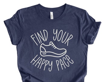 May include: Navy blue t-shirt with the text "FIND YOUR HAPPY PACE" and a white outline of a running shoe. The shirt is made of a soft material and is suitable for casual wear. The design is simple and clean, perfect for runners and fitness enthusiasts.