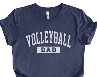 May include: Navy blue t-shirt with white text that reads "Volleyball Dad" in a collegiate font.