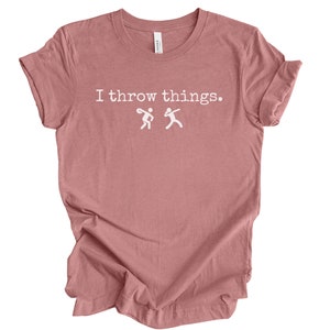 May include: A dusty rose colored t-shirt with the text "I throw things." in white. Two stick figures are shown throwing objects.