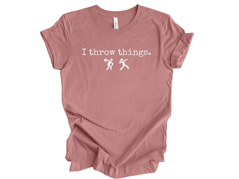 May include: A dusty rose colored t-shirt with the text "I throw things." in white. Two stick figures are shown throwing objects.