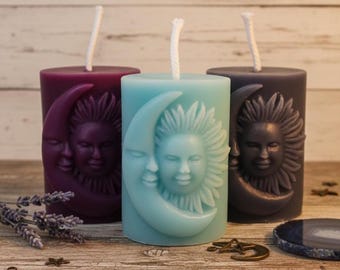 May include: Three cylindrical pillar candles in deep purple, light blue, and dark gray. Each candle features a raised relief design of a sun and crescent moon with facial features. Each candle has a single white cotton wick centered on top.
