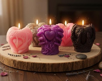 May include: A collection of decorative candles in various colors, including pink, purple, and brown, displayed on a wooden platter. Each candle has a unique design, with heart and hand motifs. The candles are lit, creating a warm ambiance.