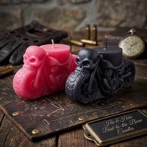 May include: Two motorcycle-shaped candles, one pink and one black, each featuring a skull design on the front. The candles sit on a leather surface with a metal nameplate that reads "His & Hers Bad-to-the-Bone Candles".