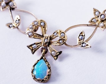 May include: A gold-toned necklace with a bow and floral design. The bow is adorned with small pearls, and a teardrop-shaped opal pendant hangs from it. The necklace features delicate floral accents with pearl details.