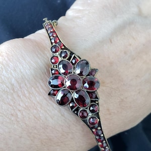 May include: An antique bracelet with a floral design. The bracelet features a series of oval and round, deep red gemstones set in a dark metal frame. The bracelet is secured with a clasp.