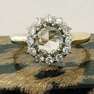 May include: A gold ring featuring a large, faceted, clear gemstone surrounded by a halo of smaller, sparkling stones. The ring's band is a simple, polished gold, and the setting is intricate, showcasing the brilliance of the gemstones.