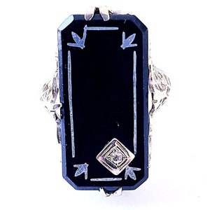May include: A rectangular black onyx ring with a diamond accent. The ring features a silver filigree design around the edges and decorative elements on the onyx surface. The ring is set against a white background.