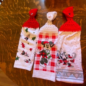 Op de afbeelding: Drie witte keukendoeken met rode en witte gehaakte ophanglussen. De handdoeken hebben een kerstthema met Mickey Mouse en Minnie Mouse-figuren.