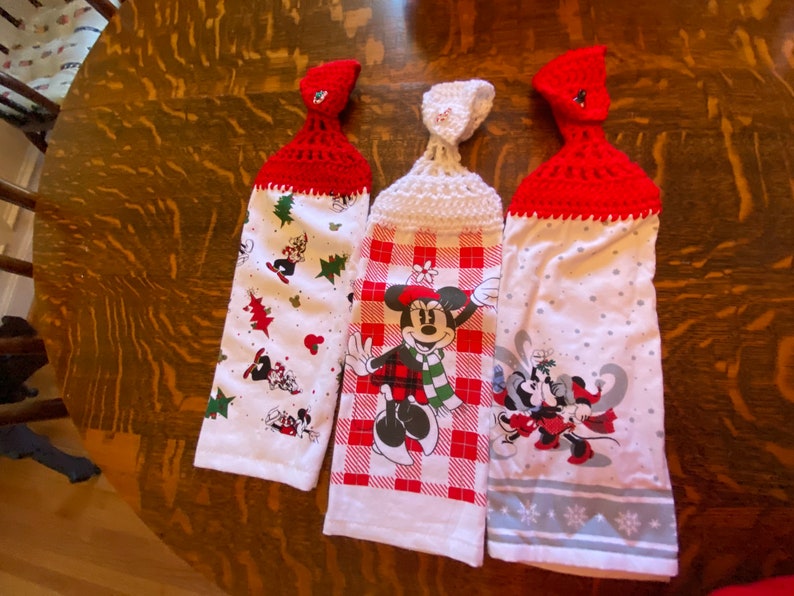Op de afbeelding: Drie witte keukendoeken met rode en witte gehaakte ophanglussen. De handdoeken hebben een kerstthema met Mickey Mouse en Minnie Mouse-figuren.