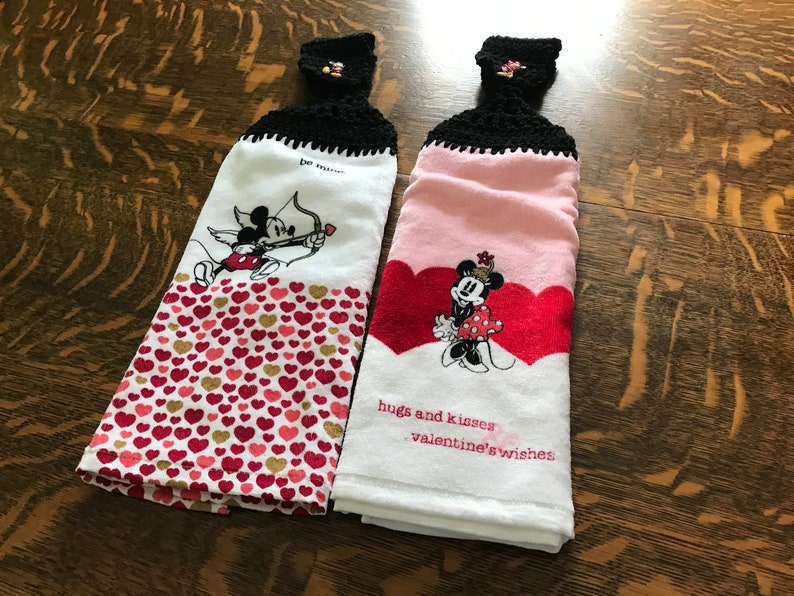 May include: Two white kitchen towels with red hearts and Mickey Mouse and Minnie Mouse Valentine's Day designs. The towels have black crocheted hanging loops and the text "hugs and kisses valentine's wishes" is on one towel.