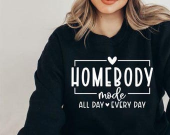May include: Black sweatshirt with white text that reads "Homebody mode all day every day" with a heart symbol between "all day" and "every day".