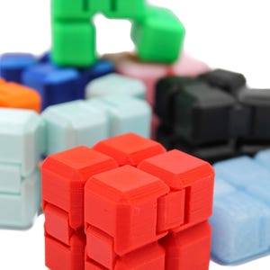 May include: A collection of multi-colored plastic infinity cube fidget toys. The cubes are composed of smaller connected square blocks in vibrant shades of red, green, blue, orange, black, and light blue, featuring visible 3D printed textures.