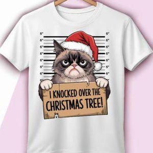 May include: White t-shirt featuring a grumpy cat wearing a Santa hat, set against a height chart background. The cat holds a sign that reads, "I Knocked Over the Christmas Tree!" A humorous holiday-themed graphic tee.