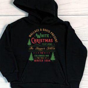 Può includere: Felpa con cappuccio nera con la scritta "WALLACE & DAVIS PRESENT WHITE CHRISTMAS FEATURING The Haynes Sisters THE COLUMBIA INN - THE TREE VT - WINTER 1954" in verde, rosso e bianco. Sono presenti anche due alberi di Natale verdi.