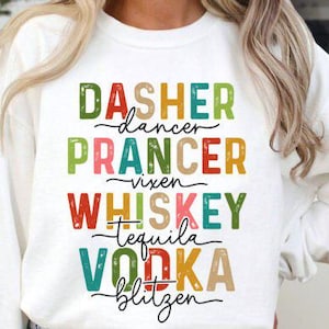 May include: White sweatshirt with colorful text. The text includes the words "Dasher, Dancer, Prancer, Vixen, Whiskey, Tequila, Vodka, Blitzen". The text is in various colors, including red, green, and orange.