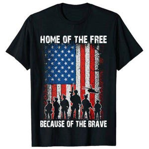 以下が含まれることがあります： アメリカ国旗のデザインと「HOME OF THE FREE BECAUSE OF THE BRAVE」の文字が入った黒いTシャツ。デザインには兵士とヘリコプターのシルエットが含まれています。