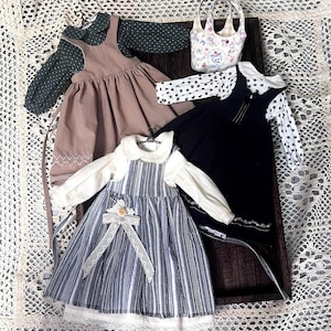Pode incluir: Tr&ecirc;s vestidos de boneca com blusas combinando. Os vestidos s&atilde;o marrom, preto e listrado azul e branco. As blusas s&atilde;o verdes com bolinhas brancas, pretas com bolinhas brancas e brancas com gola branca.